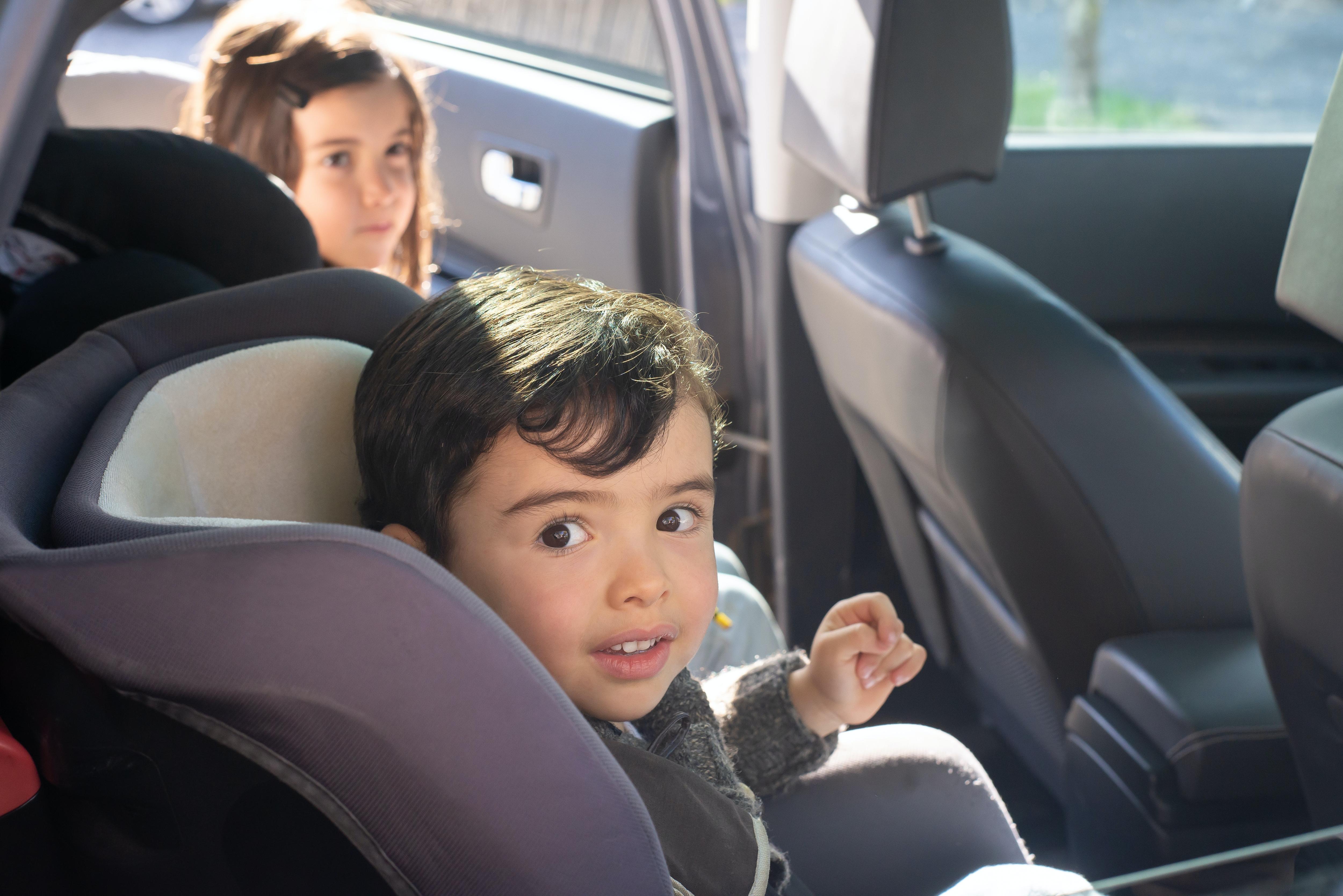 A child smiles while sitting in a child restraint in the back seat of a car.