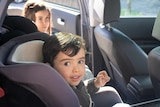 A child smiles while sitting in a child restraint in the back seat of a car.