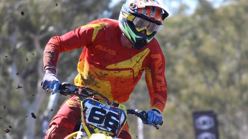 Tyler Lange dressed in his moto clothes and helmet riding through a muddy section of a course.