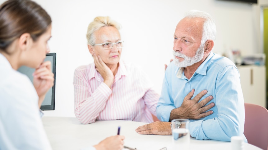 A man holds his heart and talks to his doctor. A man holds his heart and talks to his doctor.