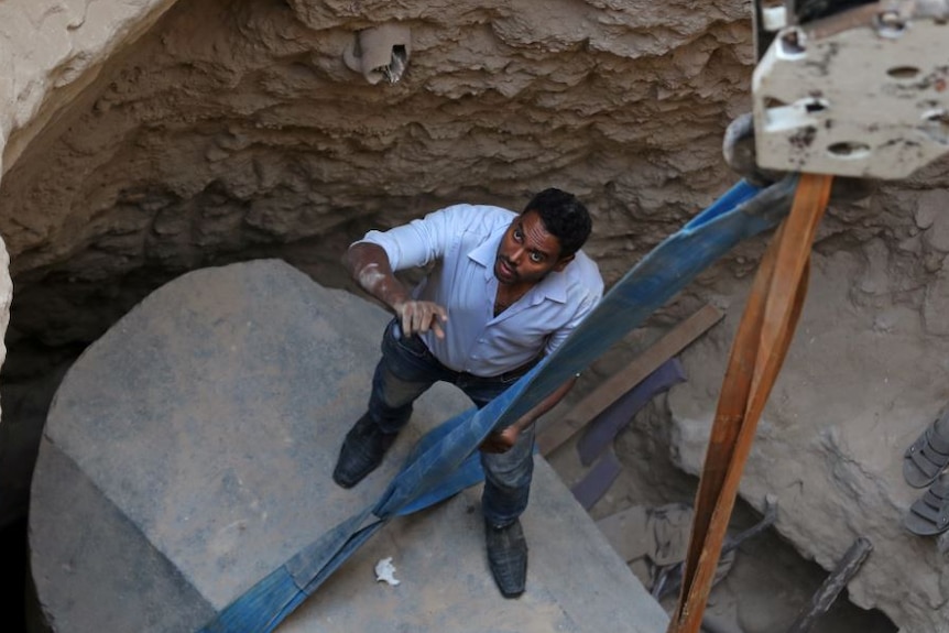Archaeologists and workers stand over a coffin containing three mummies in Alexandria