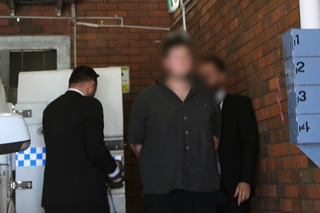 A man being led in handcuffs from a police vehicle.