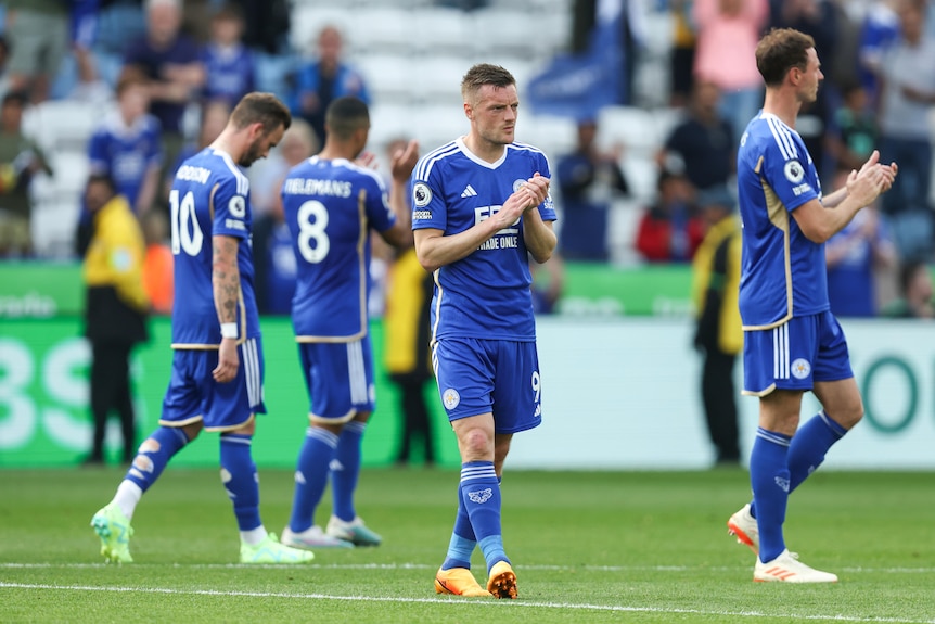 A dejected-looking Premier League player joins his teammates in applauding fans after his team is relegated. 