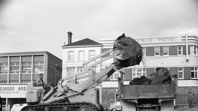 An excavator lifts dirt into a truck during construction works for the Hobart Public Library in 1960