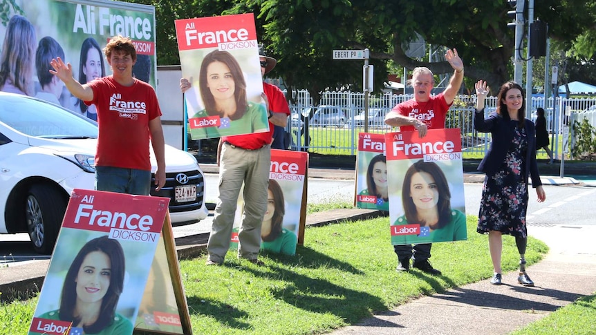 Labor's candidate for Dickson Ali France and campaign volunteers hold signs and wave at drivers.