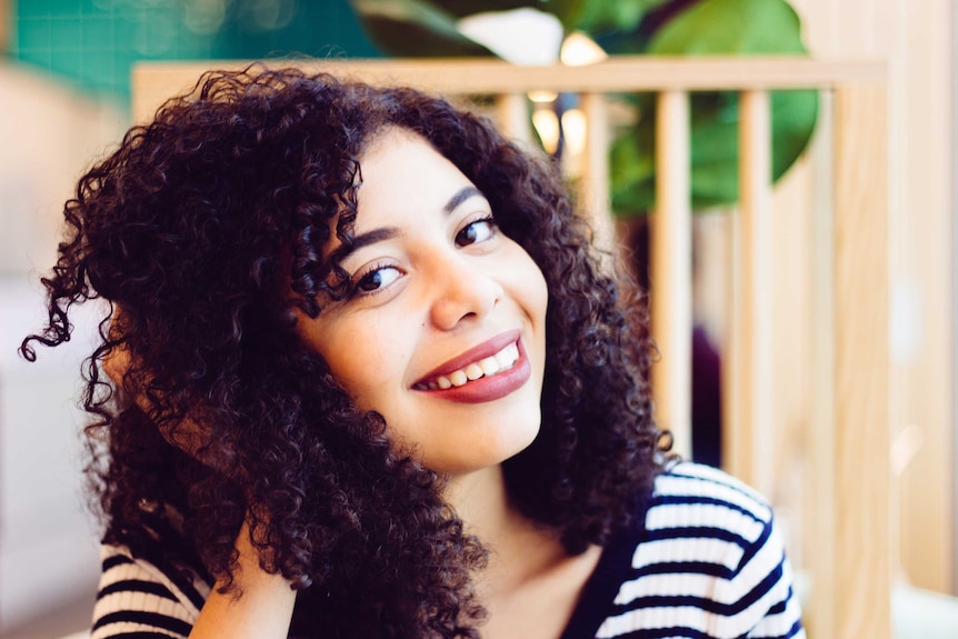 Woman with black curly hair touch her hair and smiling