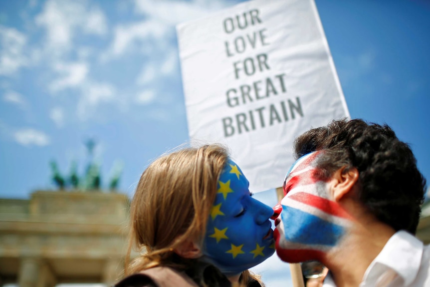 Two activists against Brexit with the EU flag and Union Jack painted on their faces kiss each other in front of Brandenburg Gate