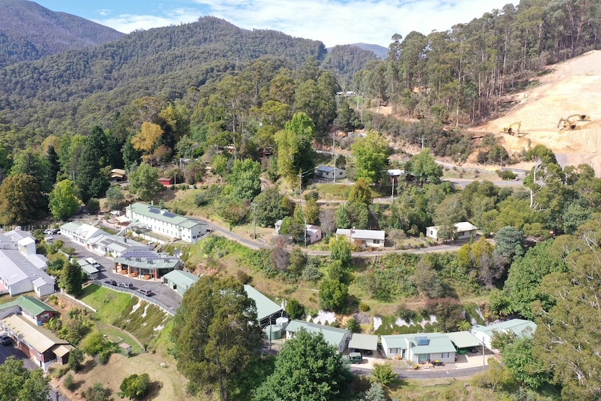 An aerial image of numerous huts and some bigger buildings nestled into a forested mountainside.