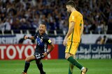 A Japanese football player celebrates while an Australian player looks downcast.