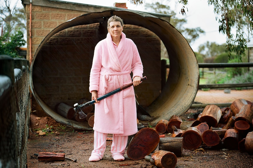 Claudias mother lisa stands in front of firewood with an axe in hand wearing pink pajamas