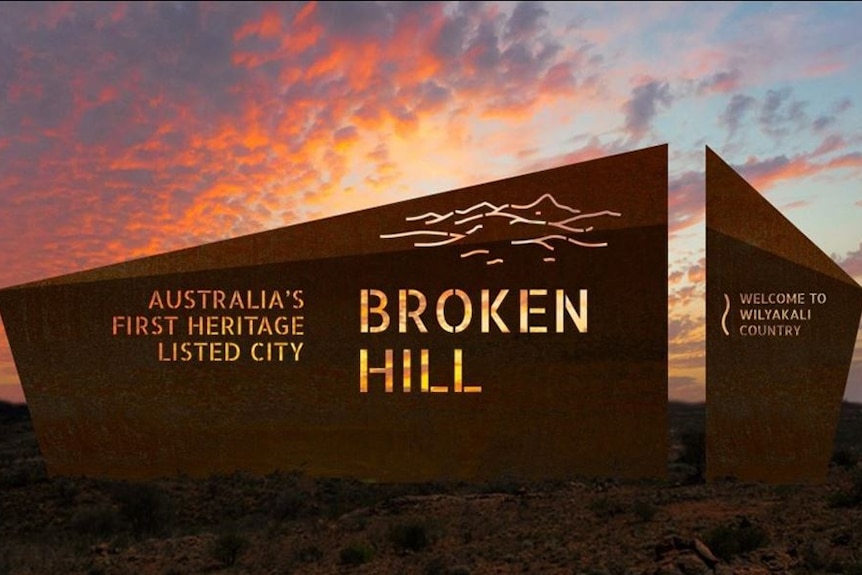 A brown sign with the words Broken Hill on it with a glowing red sunset behind it