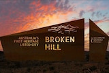 The sun glows at the death behind a sign that says "Broken Hill".