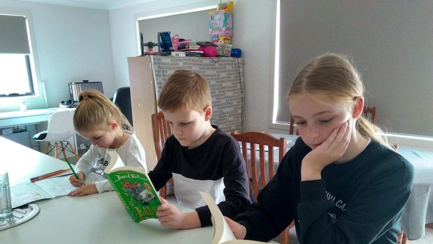 Three children at a desk at home with books.