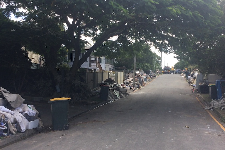 A street with piles of rubble lying in front of houses damaged by floods.