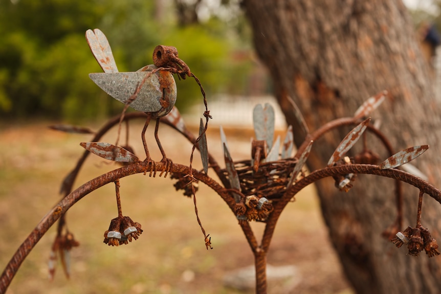 Sculpture of a bird holding a twig made from rusted wire and metal 