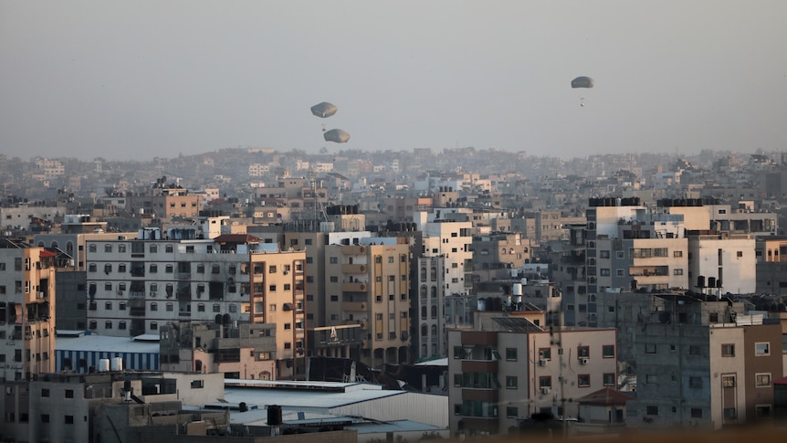 Parachutes are seen low over the skyline of a city