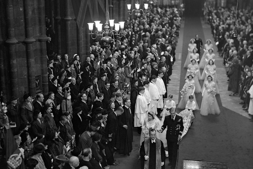 A black and white still of Queen Elizabeth walking down the aisle of Westminster Abbey with Prince Philip.