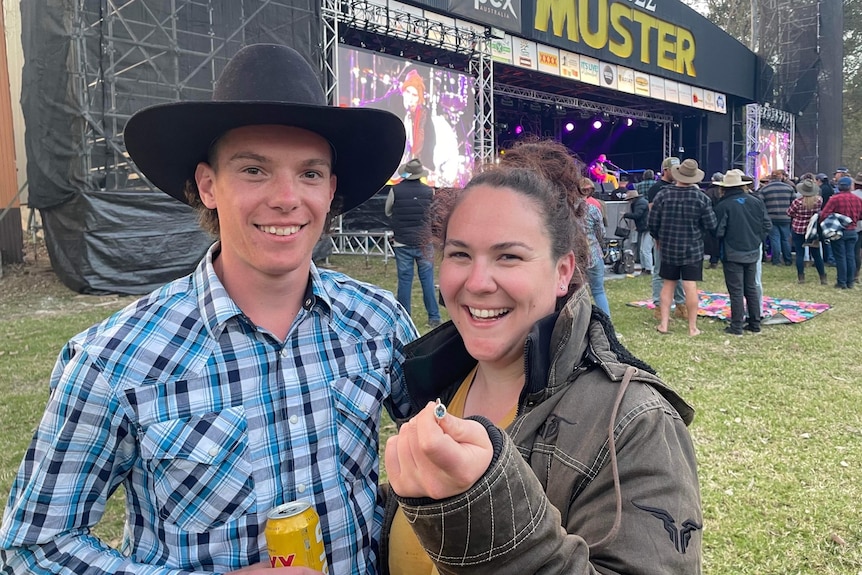 A man and a woman stand in front of the Gympie Muster stage, she is holding an engagement ring.