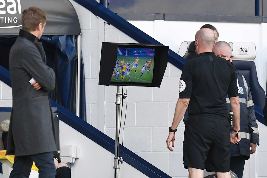 Referee Lee Mason watches a screen on the sidelines of a Premier League match. Brighton manager Graham Potter watches on.