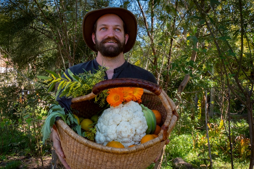 A man holds a large basket of fruit and vegetables, including a big cauliflower.