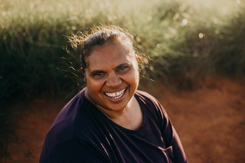 An Indigenous woman in the bush with a big smile on her face.