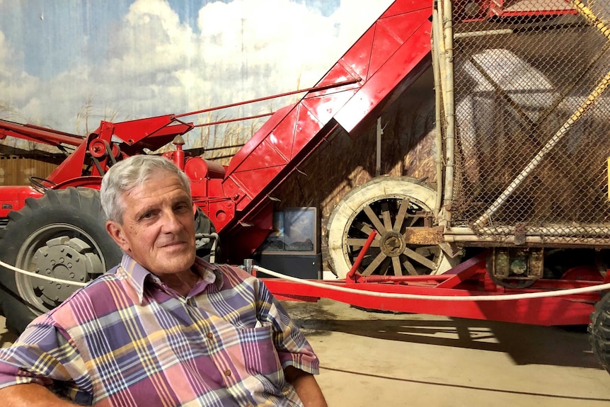 An older man sits in front of an original cane harvester on display at a museum