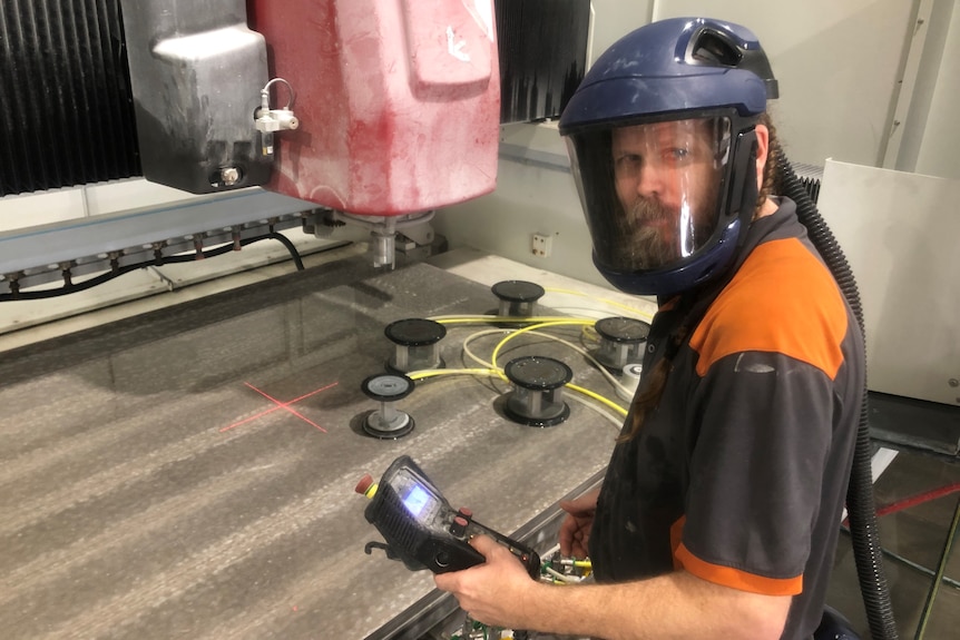 A stonemason wears full respirator with enclosed mask and hose emanating from back