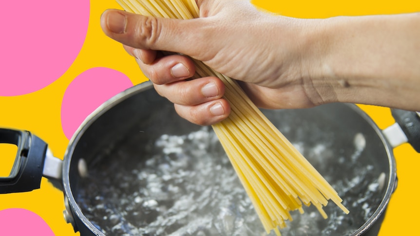 A hand puts spaghetti into a pot of boiling water.