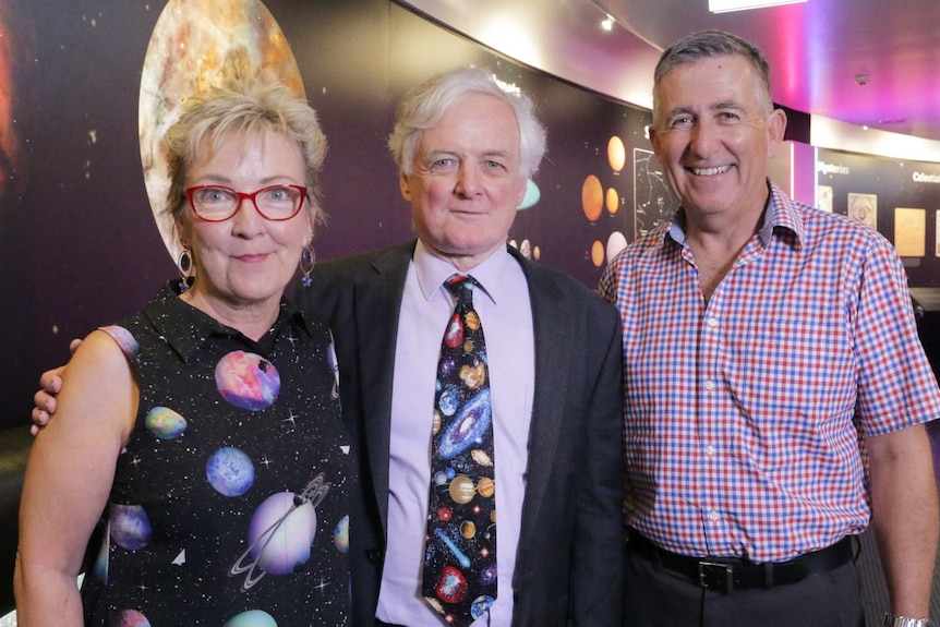 Three people smile wearing space themed clothing.