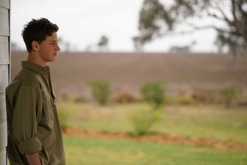 A teenager wearing a brown long sleeve shirt looks out tot he distance