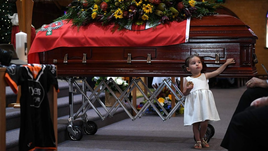 A young girl touches a large wooden casket