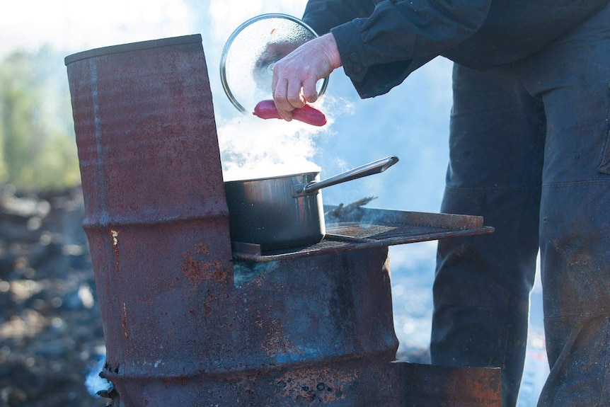 Brian cooking saveloys over a 44 gallon drum fire.