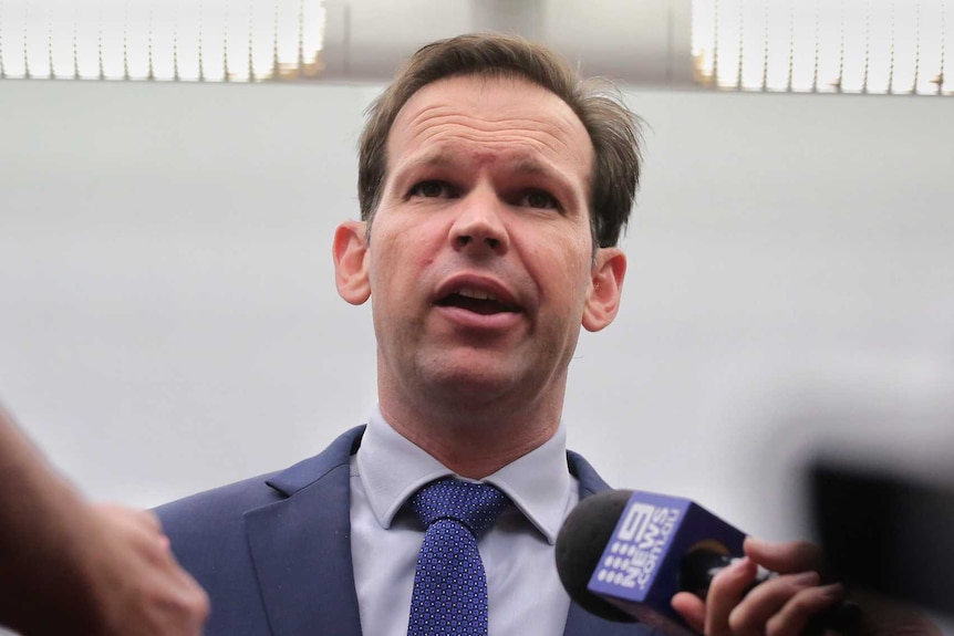 Matt Canavan clasps his hands in front of him as a media pack encircles, microphones outstretched