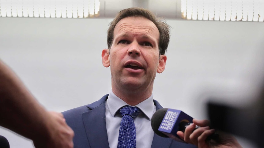 Matt Canavan clasps his hands in front of him as a media pack encircles, microphones outstretched