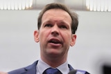 Matt Canavan clasps his hands in front of him as a media pack encircles, microphones outstretched