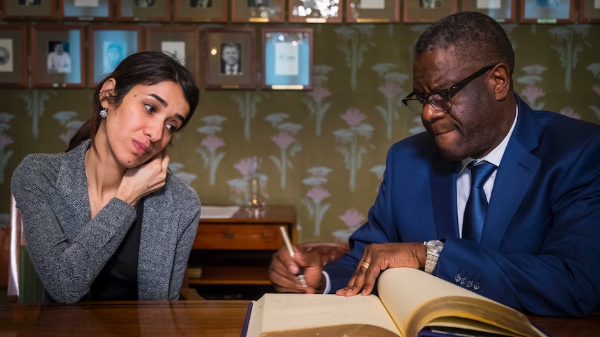 Nadia Murad and Dr Denis Mukwege sign a guestbook at the Nobel Institute in Norway with portraits lined up on a wall behind them