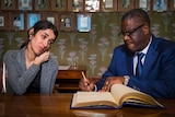 Nadia Murad and Dr Denis Mukwege sign a guestbook at the Nobel Institute in Norway with portraits lined up on a wall behind them