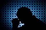 Silhouette of priest bowing head and holding cross, against blue and black background.