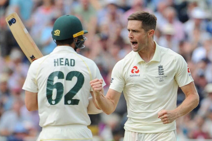England bowler Chris Woakes pumps his fist as he runs past Australia batsman Travis Head, seen from behind.