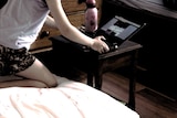 A child kneels on her bed and uses a computer
