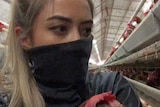 Hayley Adams inside an egg farm with a black mask carrying a chicken, some time between 2019 and 2020.