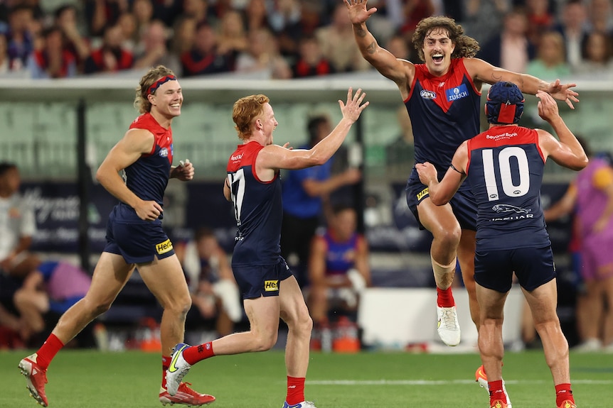 A tall AFL player grins as he leaps high in the air in celebration into the arms of his teammates.