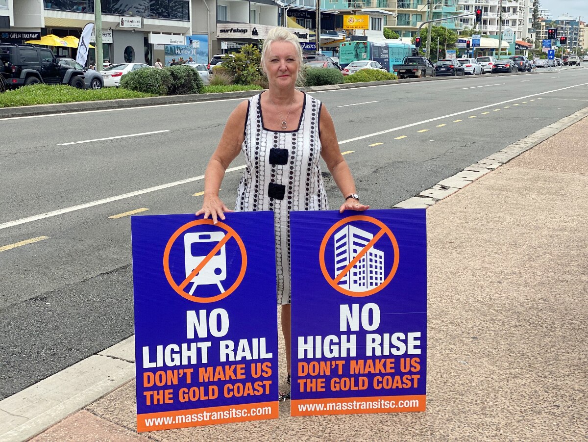 Woman with hair pulled back in ponytail stands on side of road with two signs with crosses through a tall building and phone
