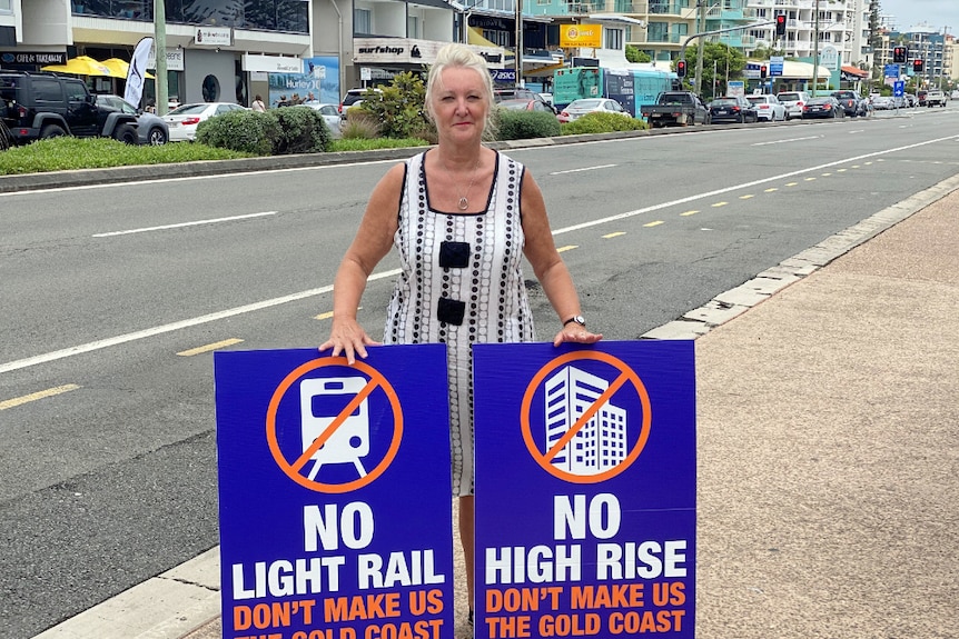 Woman with hair pulled back in ponytail stands on side of road with two signs with crosses through a tall building and phone