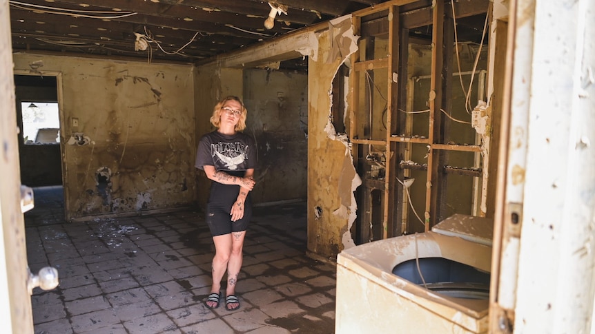 A young woman stands inside a property devastated by floodwaters.