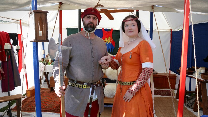 A man and women in medieval clothes stand inside a sleeping tent.