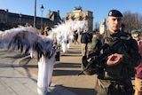 Climate change activists dressed as angels protest during climate talks in Paris, while a military officer stands nearby.
