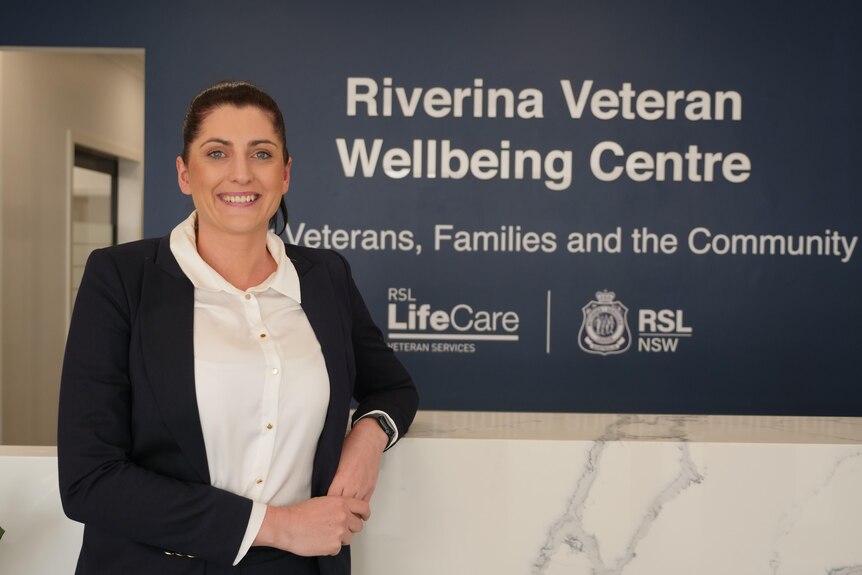 A woman smiling in front of a sign that reads 'Riverina Veteran Wellbeing Centre, Veterans, Families and the Community'