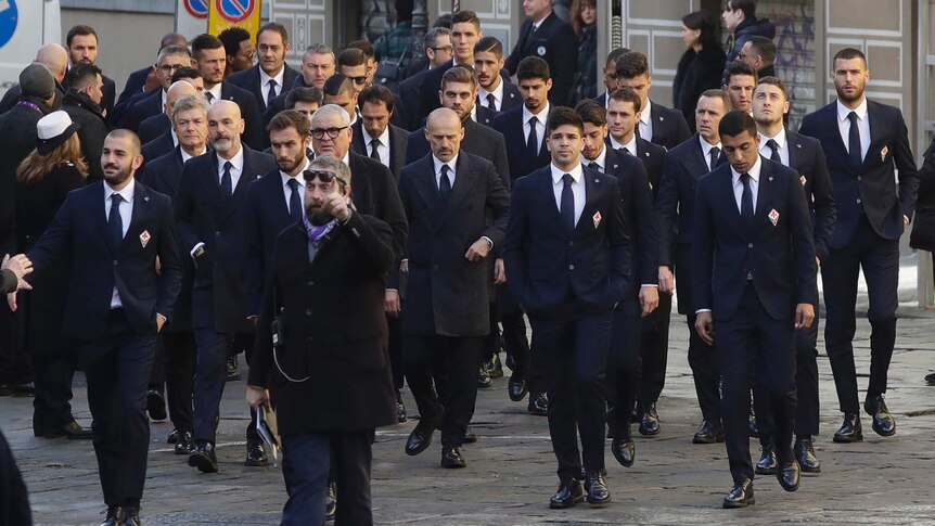 A large group of Fiorentina players wearing black suits walk together.