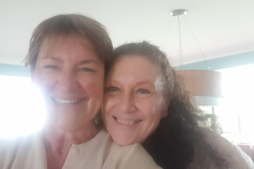 Two middle aged women leaning together with big smiles
